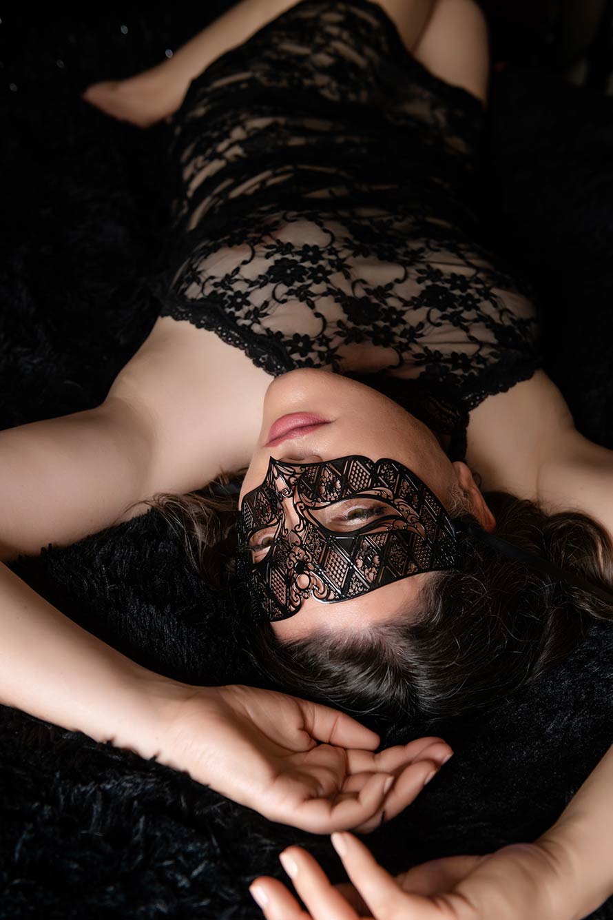 woman in a black mask wearing black lace lingerie lays on a bed