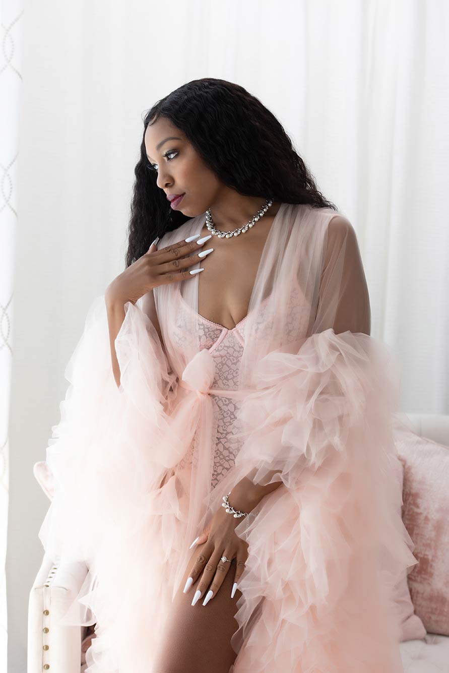 beautiful dark skinned woman wearing a pink ruffle robe looks out the window